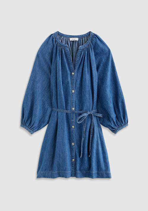 A blue denim long-sleeve mini dress with a button-up front, gathered smocked shoulders, and a matching fabric tie belt at the waist, shown against a light gray background.
