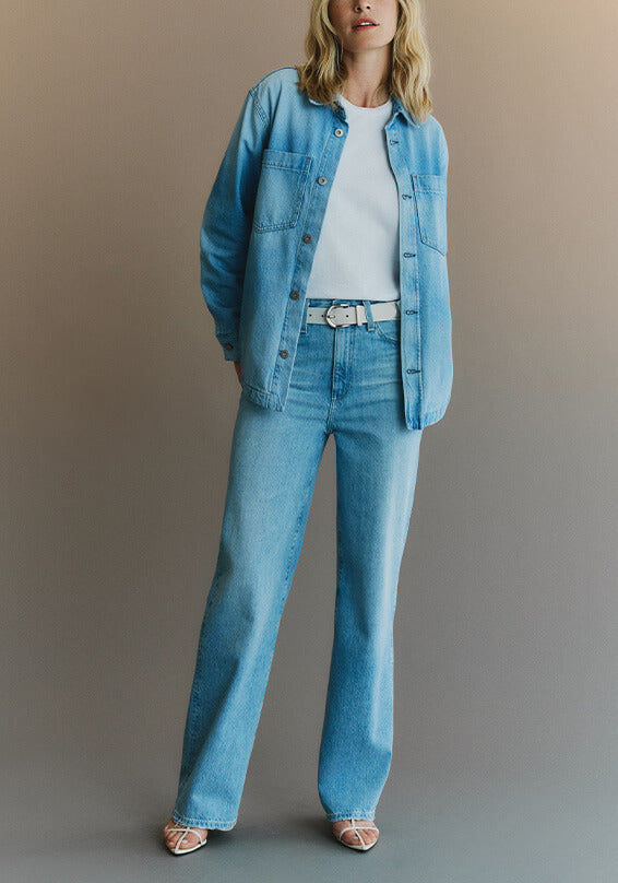 Person wearing a light jacket, white shirt, and wide-leg jeans on a plain background