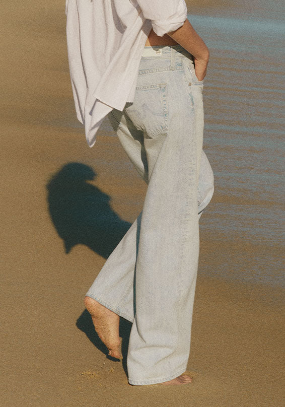 Person wearing light washed jeans and a white shirt on a sandy surface