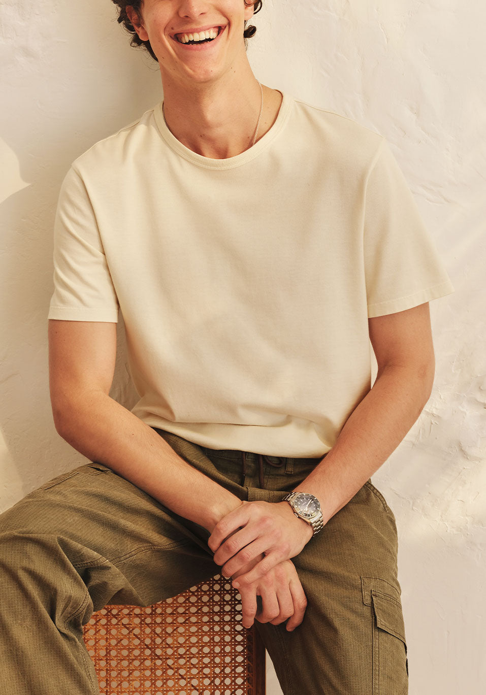 Person wearing a beige t-shirt and green pants sitting against a neutral background