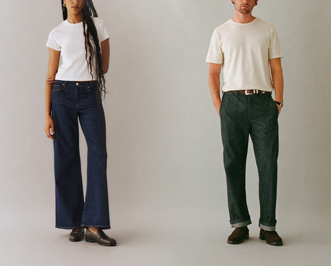Two models standing side by side wearing plain white crewneck t-shirts and wide-leg jeans, one in dark blue denim and the other in dark green denim, against a neutral light gray background.