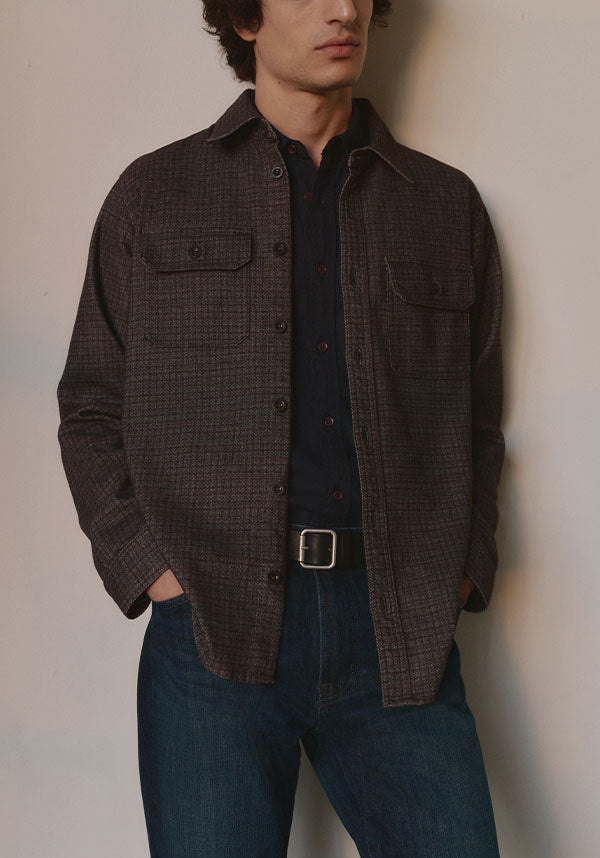 Model wearing a brown, tweedy houndstooth shirt over a dark button-up and jeans
