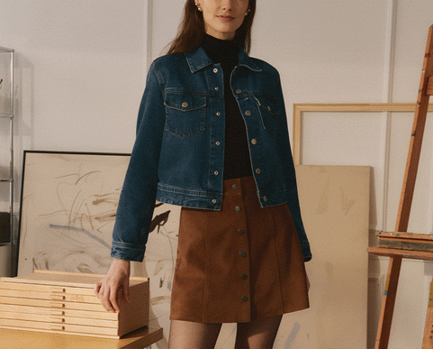 Two models in an art studio. Left is wearing a denim jacket with a turtleneck and brown skirt. Right is wearing a corduroy jacket with a denim button-up and green pants