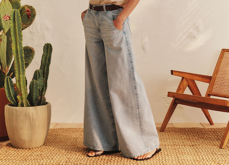 Person wearing wide-leg jeans standing next to a potted cactus indoors.